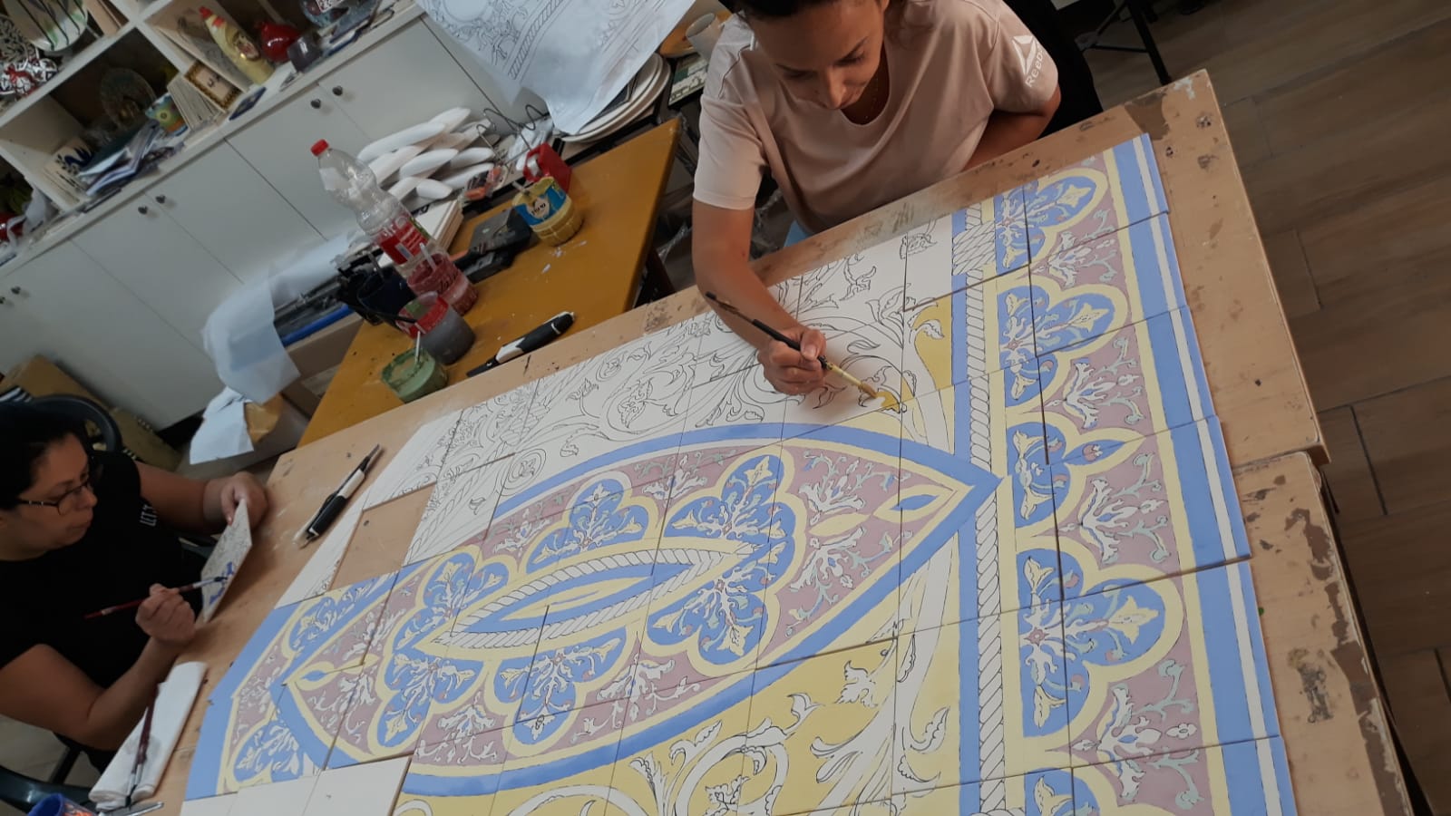 Two painters applying colour to the ceramic tiles in the Sandrouni workshop.