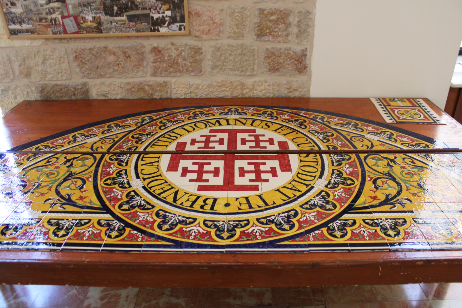 Completed glazed ceramic tiles arranged on a table, showing a red Jerusalem cross and floral decoration.