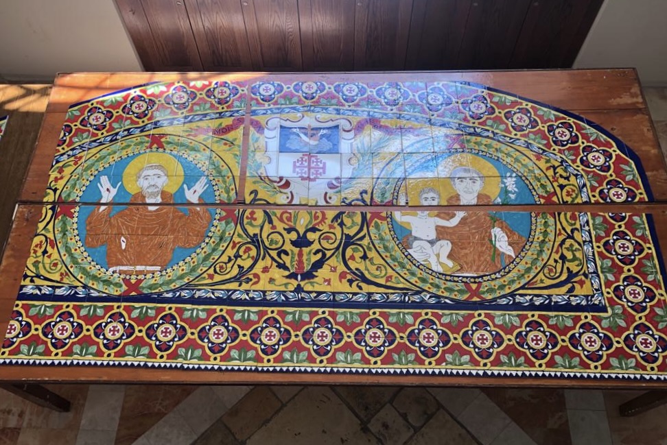 Completed ceramic panel depicting Saint Francis and Saint Anthony, arranged on a workshop table.