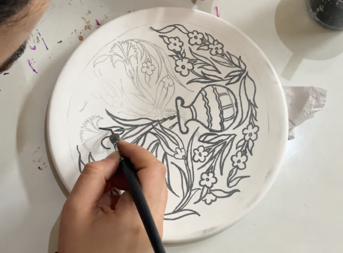 A workshop participant painting a pomegranate and floral design on a ceramic plate